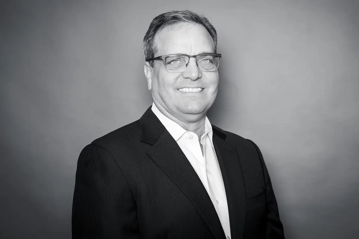A professional man in a suit and glasses posing for a black and white photo.