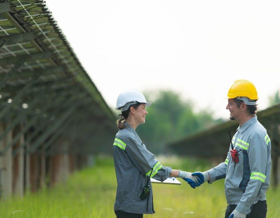 Two energy professionals shaking hands in front of a solar farm, representing successful collaboration and partnership in renewable energy.