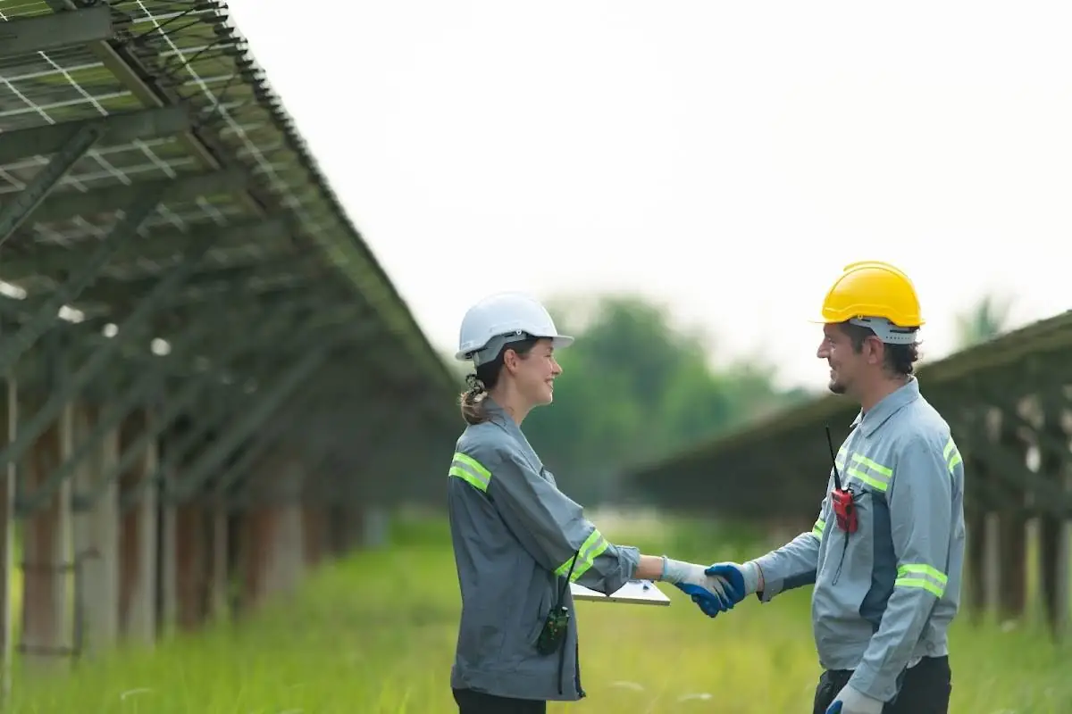 Two energy professionals shaking hands in front of a solar farm, representing successful collaboration and partnership in renewable energy.