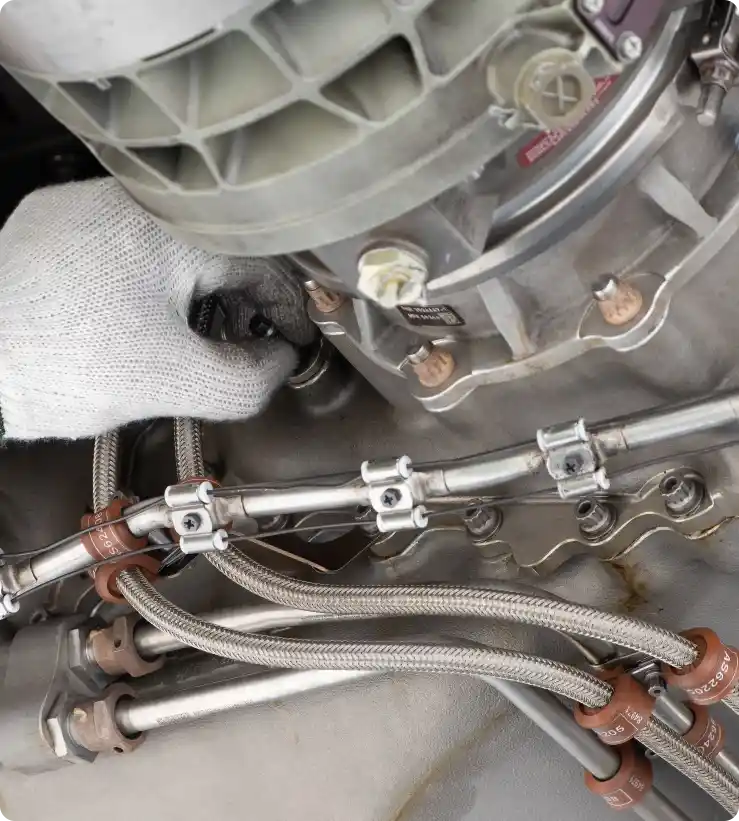 A hand in gloves holds a hose on a jet engine, ensuring proper maintenance and safety.