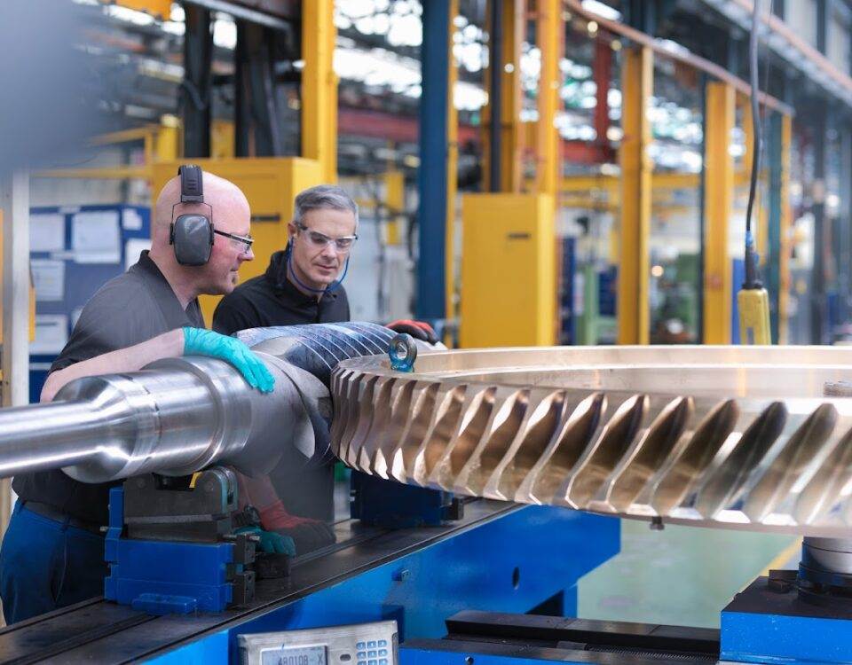 Two engineers inspecting and working on a large turbine component in a workshop, showcasing precision and expertise in turbine maintenance.