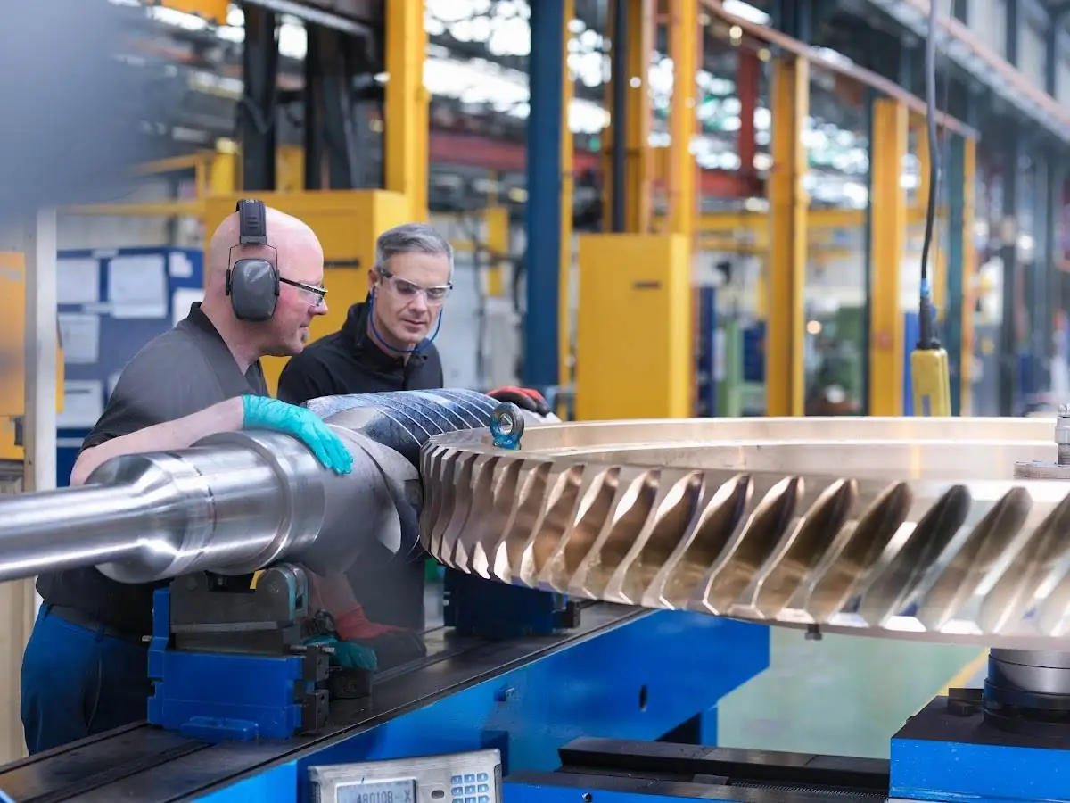 Two engineers inspecting and working on a large turbine component in a workshop, showcasing precision and expertise in turbine maintenance.