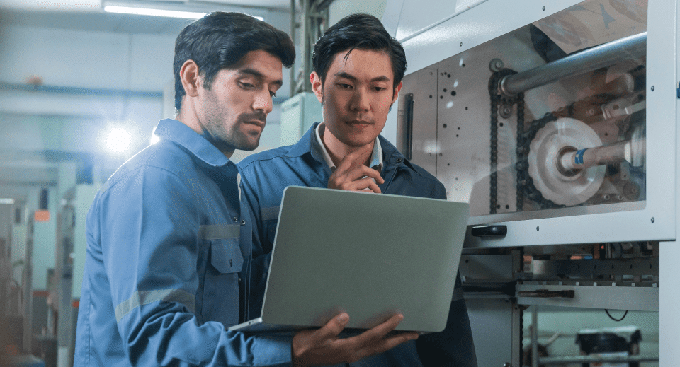 Two men in blue shirts focused on a laptop screen, engaged in a discussion or work-related activity.