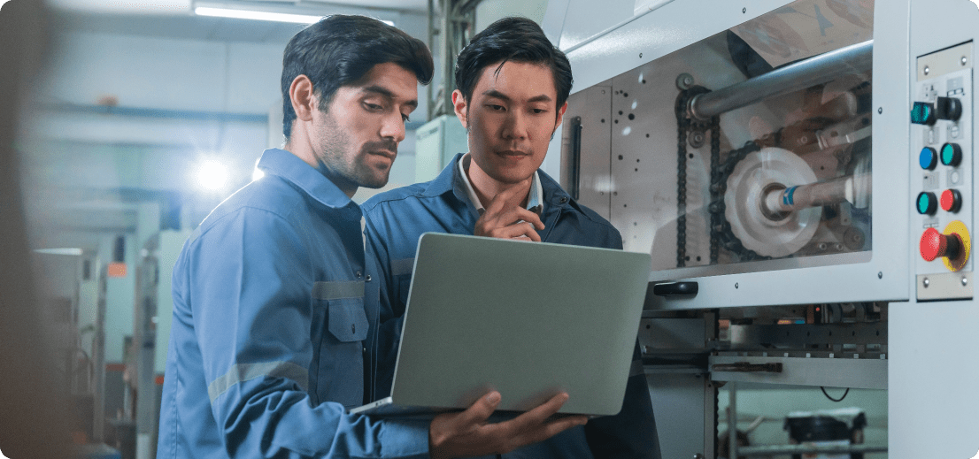 Two men in blue shirts focused on a laptop screen, engaged in a discussion or work-related activity.