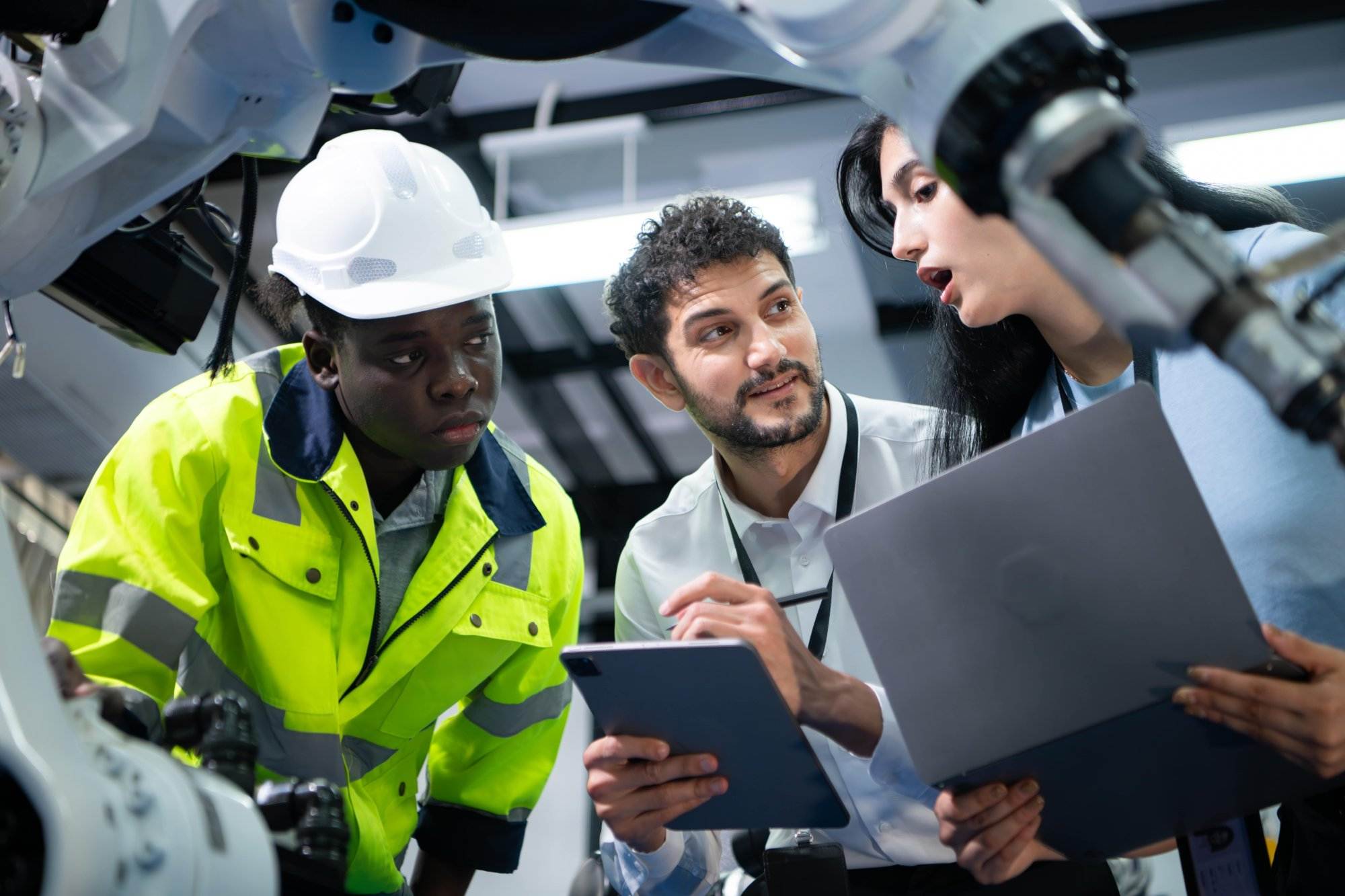 Technicians examine and discuss the functionality of industrial hand robots in a high-tech workshop.