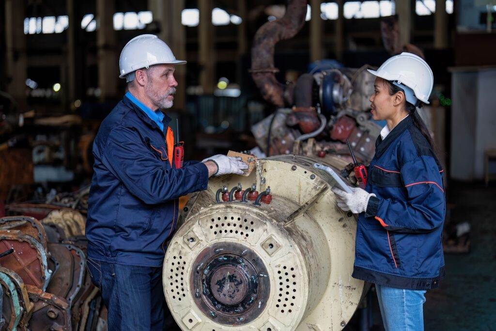 Two engineers in protective gear working on a turbine control mechanism in an industrial setting